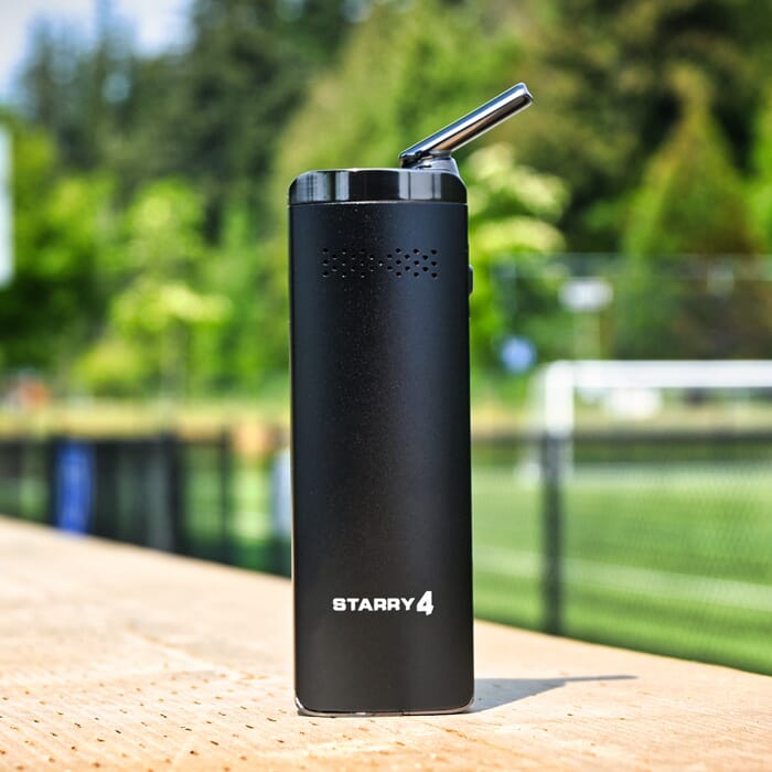 The Starry V4 vaporizer from XMax standing on a path next to a football field.